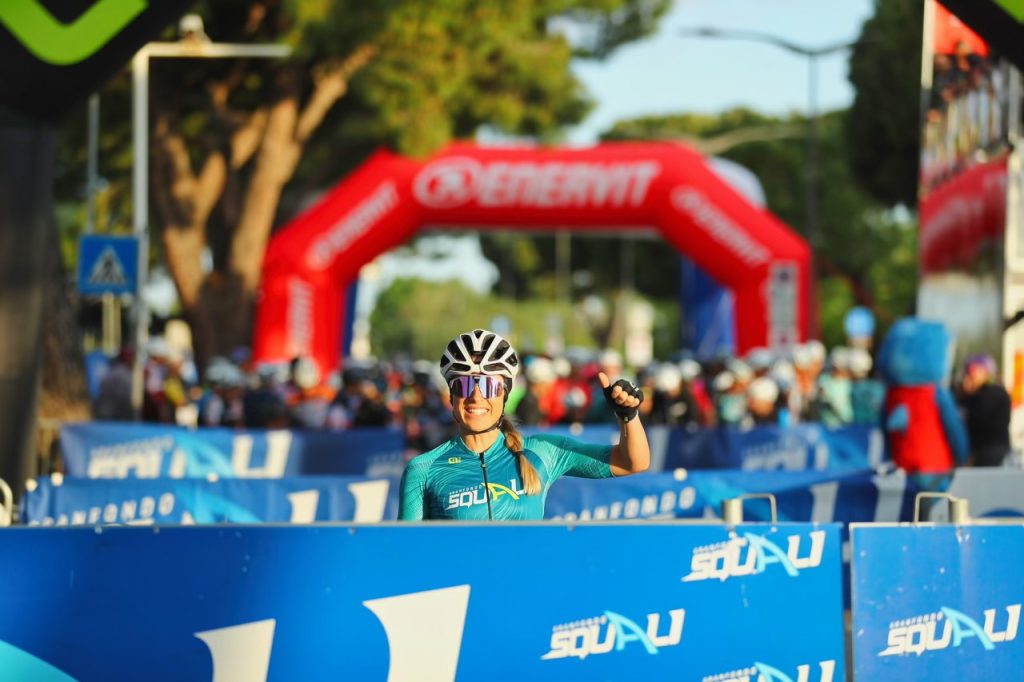 Primo piano di una ciclista sorridente in griglia di partenza con la maglia tecnica ufficiale della Granfondo Squali.