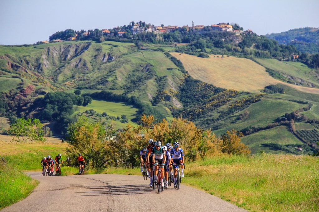 Un gruppo di ciclisti in salita durante la Granfondo Squali con un antico borgo collinare sullo sfondo.