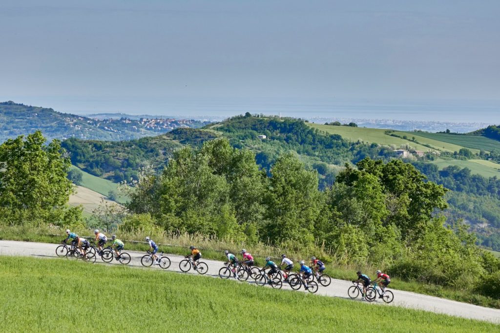 Ampia veduta panoramica di un gruppo di ciclisti che pedala sulle colline tra Romagna e Marche.