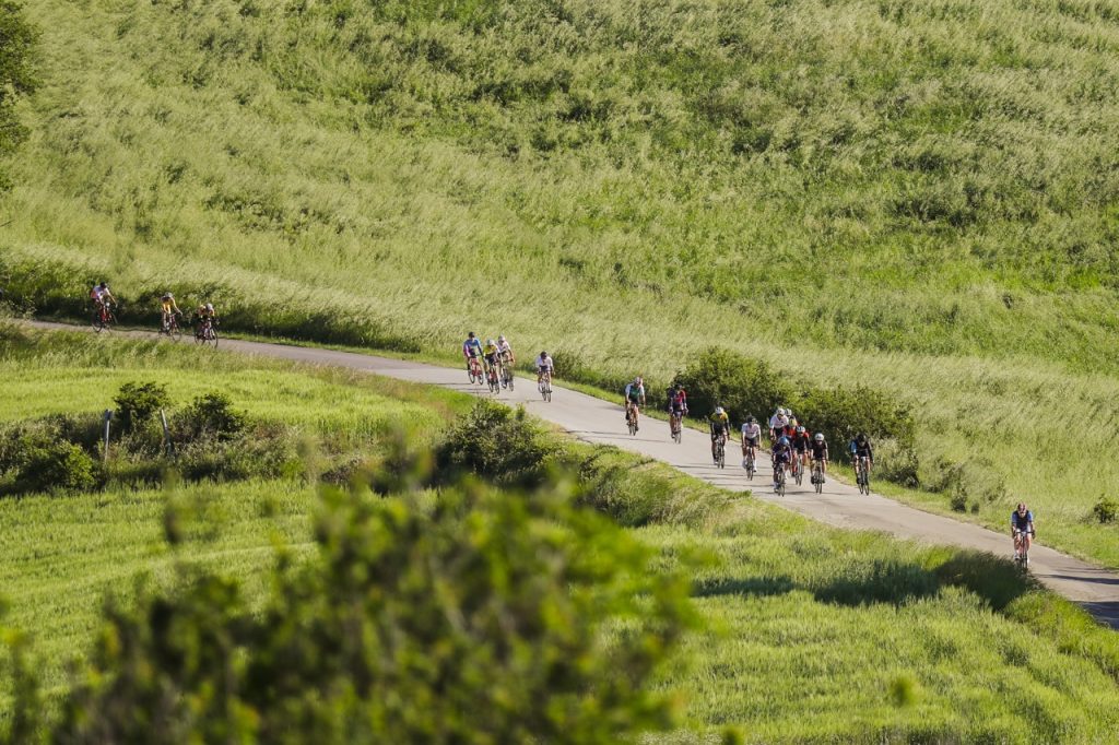 Ciclisti in gruppo lungo un tratto pianeggiate immerso nel verde del percorso Nove Colli