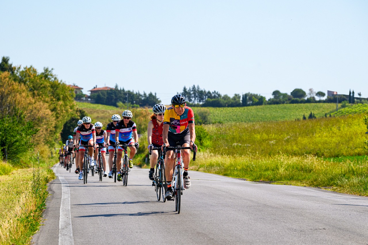 Una guida ciclistica dei Riccione Bike Hotels conduce un gruppo di cicloturisti su strada nell'entroterra romagnolo