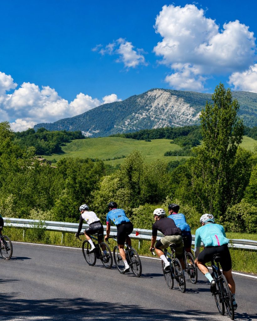 Gruppo di ciclisti su strada pedala verso il massiccio del Monte Carpegna