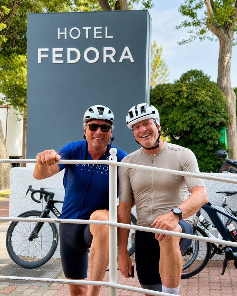 Ciclisti su strada davanti al cartello dell'Hotel Fedora a Riccione