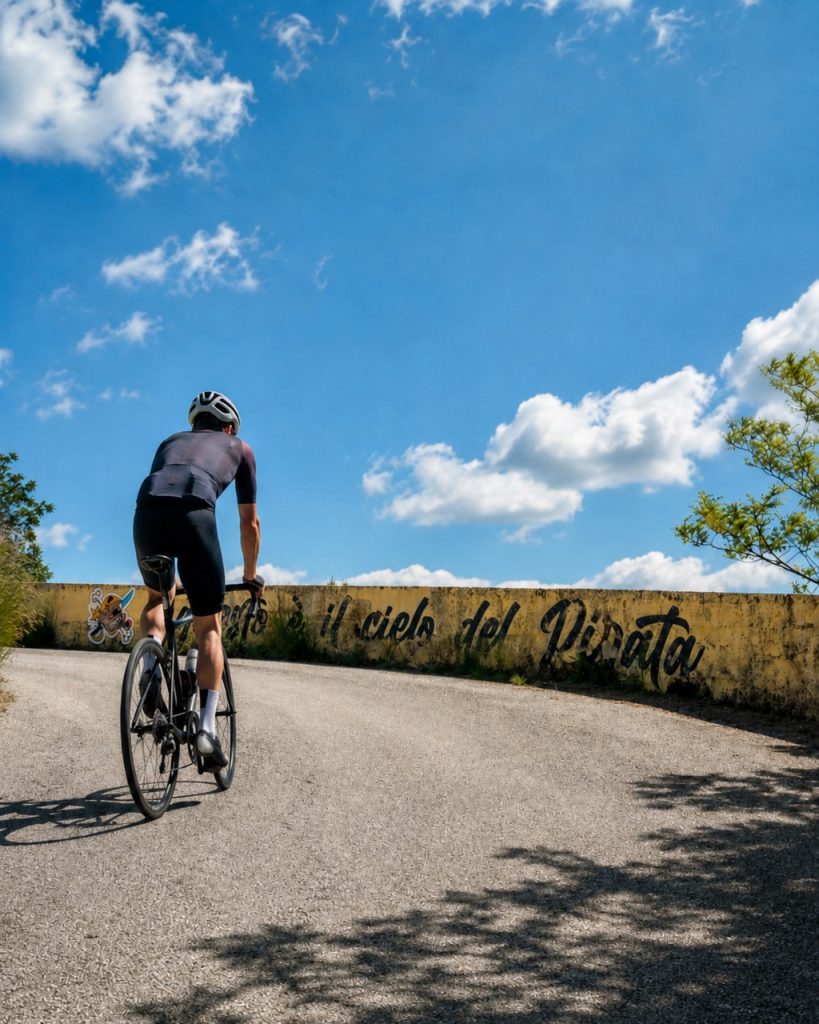 Ciclista in bici da corsa affronta i tornanti della salita del Cippo di Carpegna con scritte per Pantani