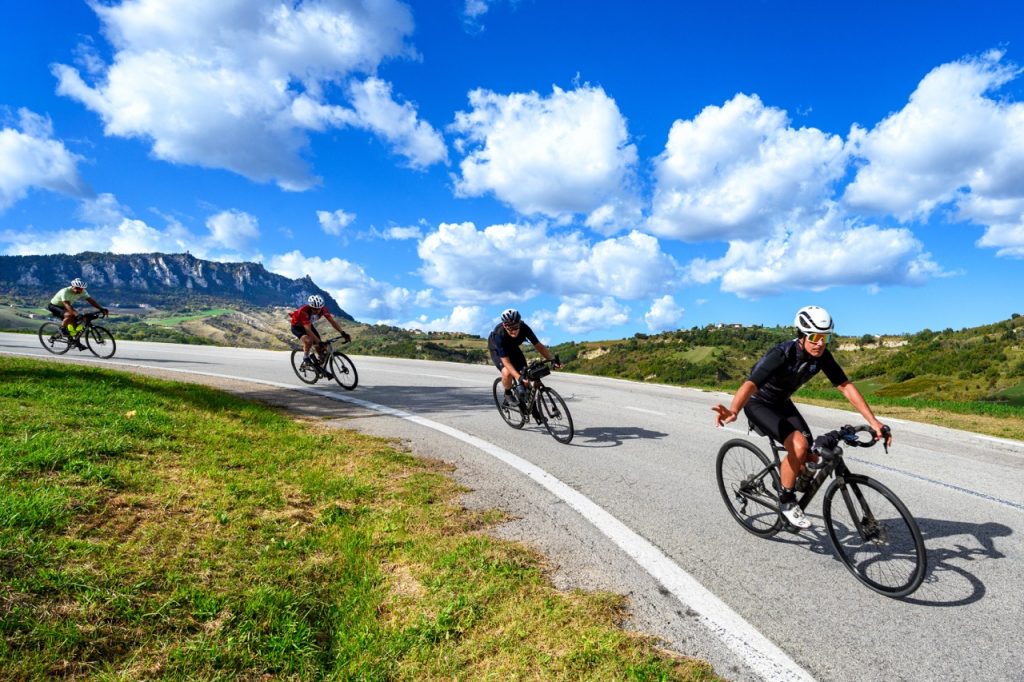 Un gruppo di ciclisti con guida Riccione Bike Hotels in bici sulla discesa da San Marino con sfondo il Monte Titano