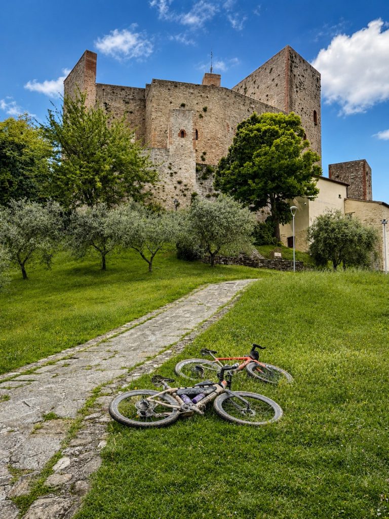 Two gravel bikes leaning on the grass along a stone path at the foot of the majestic Malatesta Fortress in Montefiore Conca